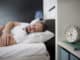 Man sleeping in his bedroom with alarm clock in foreground. It’s morning