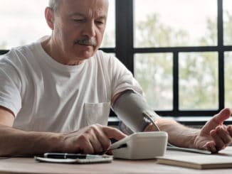 Old hispanic man feeling bad using a home blood pressure machine to check his health in the morning