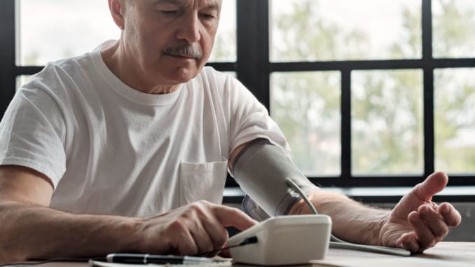 Old hispanic man feeling bad using a home blood pressure machine to check his health in the morning