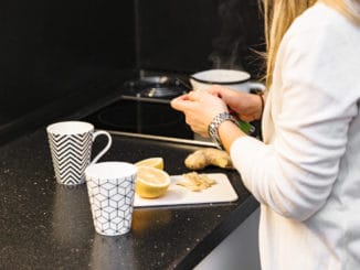Woman in kitchen slicing lemon and ginger to make some tea for guests