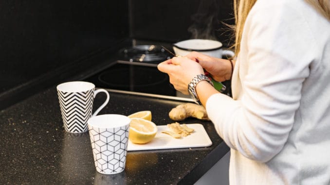 Woman in kitchen slicing lemon and ginger to make some tea for guests