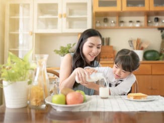 Asian mothers and daughters pour milk together. There is a bread with butter next to it for breakfast.