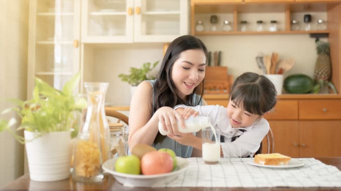 Asian mothers and daughters pour milk together. There is a bread with butter next to it for breakfast.