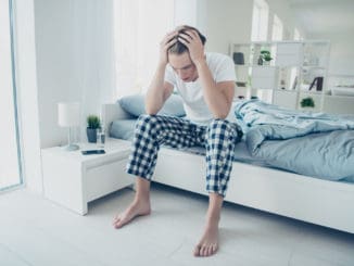Full size photo of fatigue exhausted man have terrible migraine headache, after party suffer hangover catch cold influenza virus wear checkered plaid pajama sit on bed in house indoors