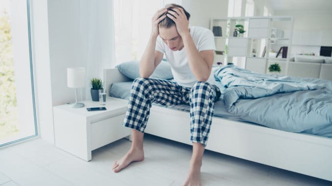 Full size photo of fatigue exhausted man have terrible migraine headache, after party suffer hangover catch cold influenza virus wear checkered plaid pajama sit on bed in house indoors