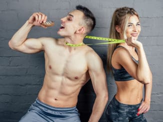 Beautiful blonde women in camouflage sports suit inflated and beautiful men with a measuring tape in the gym eating an orange and biscuits.