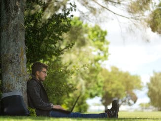 Man sitting under a tree, reposing and working on his computer.
