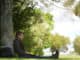 Man sitting under a tree, reposing and working on his computer.