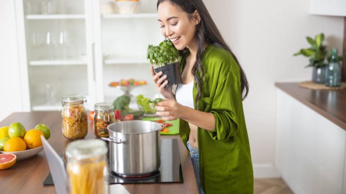 Smiling modern young housewife looking into the cooking pot