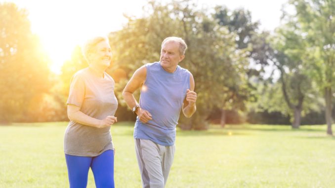 Healthy senior couple jogging in park with yellow lens flare in background