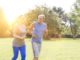 Healthy senior couple jogging in park with yellow lens flare in background