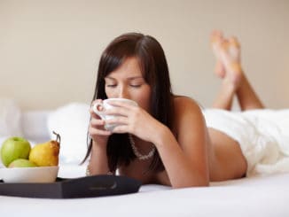 Young beautiful woman drinking coffee lying on white bed