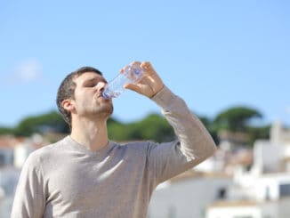 Casual adult man drinking bottled water standing in a rural town a sunny day