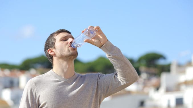 dreamstime_m_168241688 Casual adult man drinking bottled water standing in a rural town a sunny day
