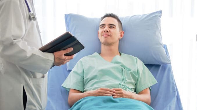 Young caucasian male patient on bed talking to doctor in hospital room, Health care and insurance concept