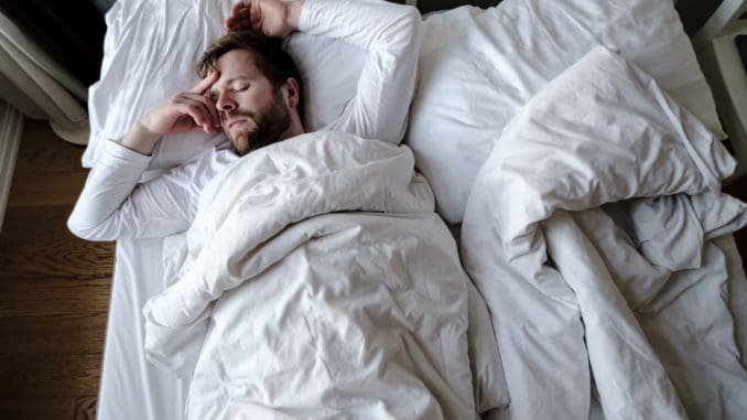 Bearded man sleeps restlessly in bed, he is alarmed and had a terrible nightmare.