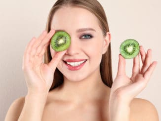 Young woman with cut kiwi on beige background. Vitamin rich food