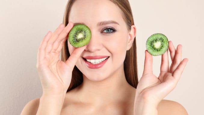 Young woman with cut kiwi on beige background. Vitamin rich food