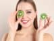 Young woman with cut kiwi on beige background. Vitamin rich food