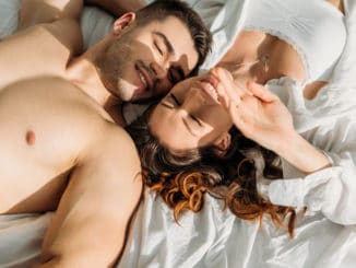 Top view of happy, couple smiling with closed eyes while lying in bed together