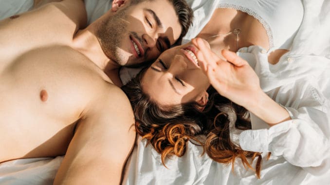 Top view of happy, couple smiling with closed eyes while lying in bed together