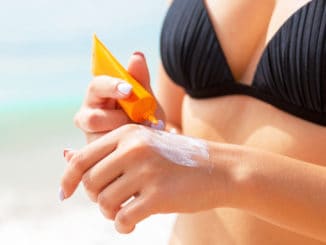 Tanned girl is using sunscreen on her hand at the beach