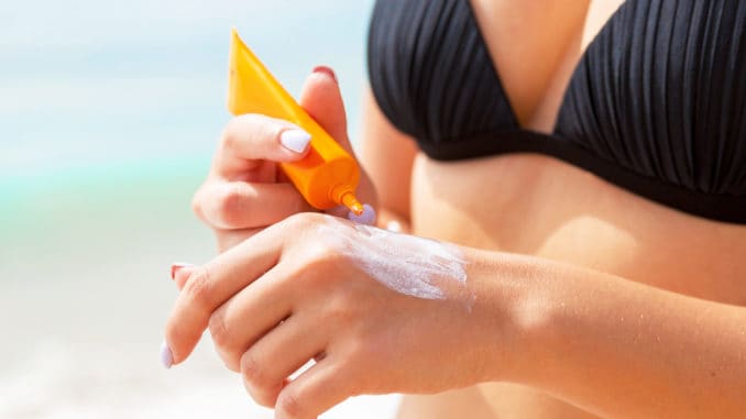 Tanned girl is using sunscreen on her hand at the beach