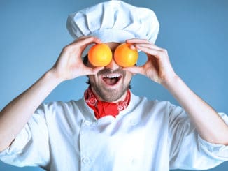 Portrait of a man cook holding oranges. Shot in a studio over grey background.