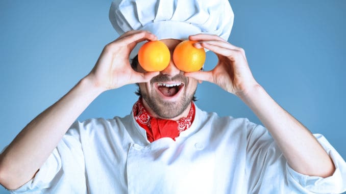 Portrait of a man cook holding oranges. Shot in a studio over grey background.