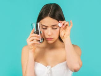 Young woman taking pill against headache. Brunette taking a pill with a glass of water. Woman taking drugs to releave