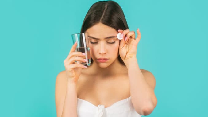 Young woman taking pill against headache. Brunette taking a pill with a glass of water. Woman taking drugs to releave