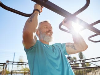 Strong and healthy people. Happy bearded senior man pulling up on horizontal bar and smiling while training outdoors. He is working out at the stadium. Fitness, sport, workout, healthy lifestyle