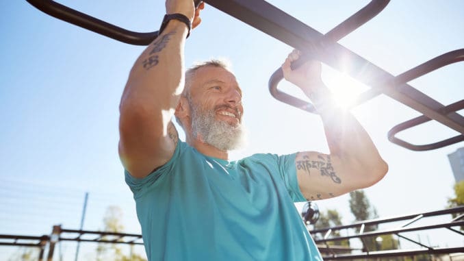 Strong and healthy people. Happy bearded senior man pulling up on horizontal bar and smiling while training outdoors. He is working out at the stadium. Fitness, sport, workout, healthy lifestyle