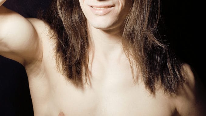 Handsome young man with long hair naked torso on black background smiling