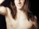 Handsome young man with long hair naked torso on black background smiling