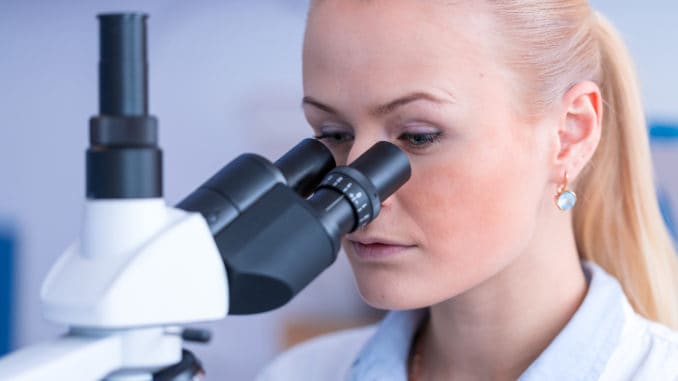 Girl with a slide for the microscope University Hospital. Attractive young scientist looking at the microscope slide in the forensic laboratory.