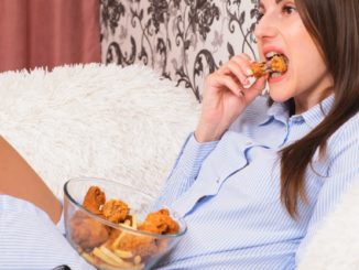 Young happy woman eating deep fried chicken, closeup. Woman eats chicken wings, calorie intake and health risks, cholesterol.