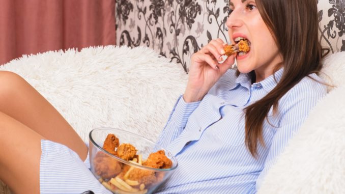 Young happy woman eating deep fried chicken, closeup. Woman eats chicken wings, calorie intake and health risks, cholesterol.
