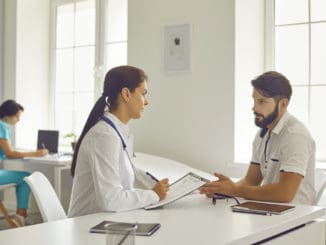 Medical clinic offfice. Young smiling woman doctor in medical uniform sitting and listening to talking man patient during consultation. Visiting doctor in hospital concept