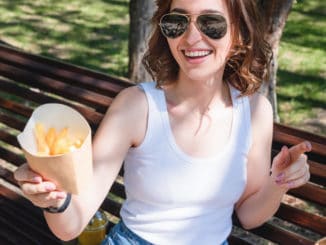 Beautiful, young woman eating fries in the street. The concept of fast food, food delivery and lunch in nature.