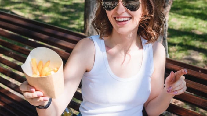 Beautiful, young woman eating fries in the street. The concept of fast food, food delivery and lunch in nature.