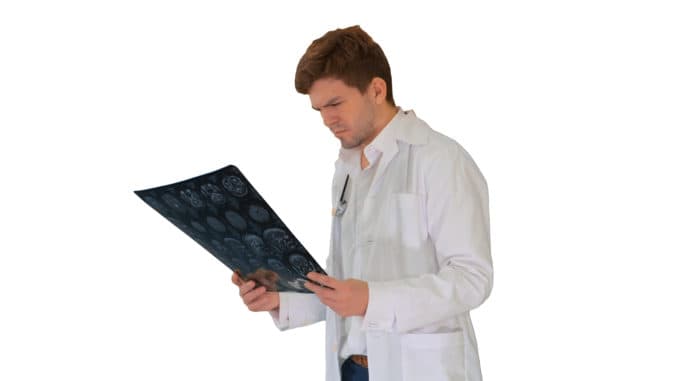 Concentrated male doctor looking at computed tomography xray image on white background.