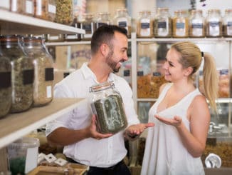 Happy women and men holding glass can with dried herbs in organic shop