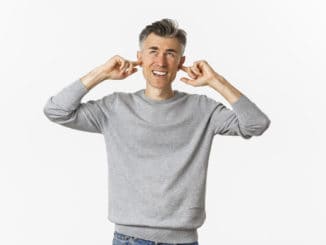 Portrait of annoyed middle-aged man complaining on loud neighbours, shut ears with fingers and looking up bothered by disturbing noise, standing over white background.