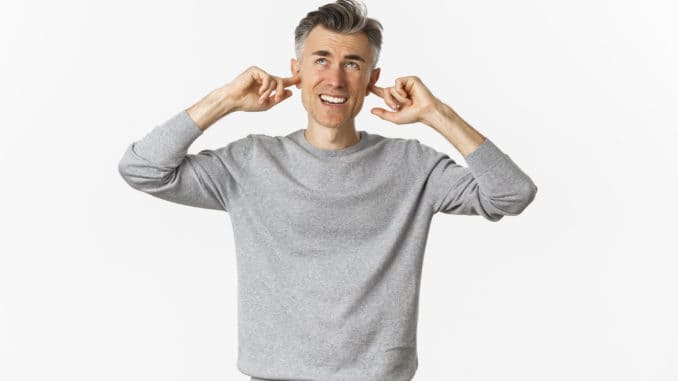 Portrait of annoyed middle-aged man complaining on loud neighbours, shut ears with fingers and looking up bothered by disturbing noise, standing over white background.