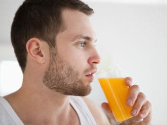 Close up of a healthy man drinking orange juice in his kitchen