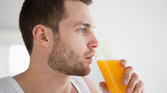 Close up of a healthy man drinking orange juice in his kitchen