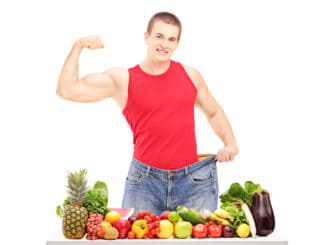 Weight loss man showing his muscles and standing behind a pile of fruits and vegetables, isolated on white background