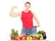 Weight loss man showing his muscles and standing behind a pile of fruits and vegetables, isolated on white background