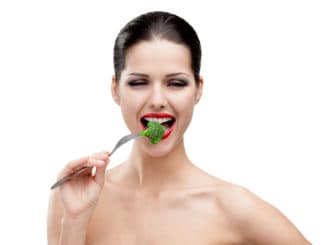 Woman with red lipstick eating broccoli on the stainless fork, isolated on white. Fresh and healthy dieting food